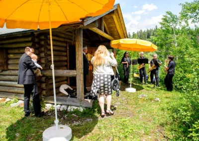 Hochzeitsreportage bei Holzhutte am Eibsee, Musiker spielen draussen unter gelben Sonnenschirmen.