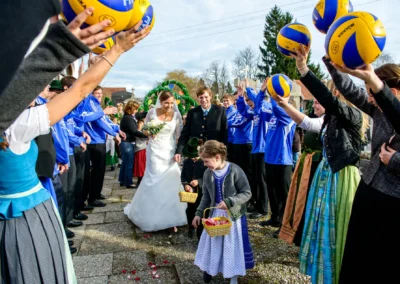 Brautpaar unter blauen Volleyballbögen bei kirchlicher Trauung nahe Holzkirchen, eingehüllt in freudige Hochzeitsreportage.
