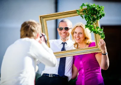 Ein Paar posiert fröhlich mit einem Bilderrahmen bei einer Hochzeit im Kloster Seeon, fotografiert im Freien.