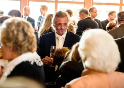Hochzeitsgast mit Sektglas bei Feier in Karlsfeld. Aufnahme von Hochzeitsfotografie zeigt lebhafte Szene.