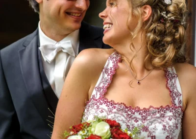 Brautpaar lacht zusammen bei einer Hochzeitsreportage am Walchensee, Brautstrauss mit roten und weissen Rosen.