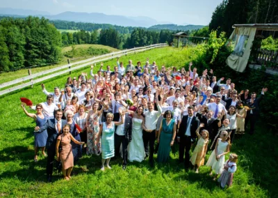 Hochzeitsgesellschaft posiert auf einer grünen Wiese, Hochzeit auf der Sprengenöder Alm in Oberbayern.