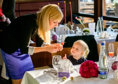 Frau interagiert mit Kind bei einer Hochzeit in Karlsfeld. Festlich gedeckter Tisch im Hintergrund. Hochzeitsfotograf.