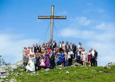Hochzeitsgesellschaft auf einem Berg mit Holzkreuz bei Kampenwand. Aufnahmen bei einer Hochzeit in Oberbayern.