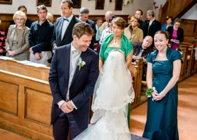 Brautpaar bei kirchlicher Trauung in Schaftlach, umgeben von Gaesten in festlicher Kleidung. Hochzeitsreportage.