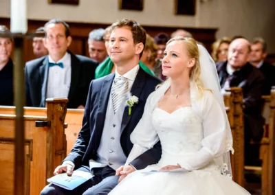 Brautpaar bei kirchlicher Trauung in Schaftlach, glücklich sitzend in einer Kirche, Hochzeitsfotografien aus München.