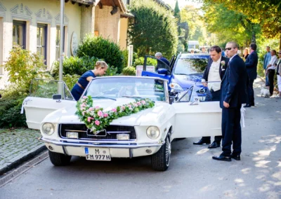 Hochzeitsfoto: Brautpaar vor Oldtimer in Starnberg, Hochzeitsautodekoration mit Blumen. Hochzeitsreportage bei Sonnenschein.