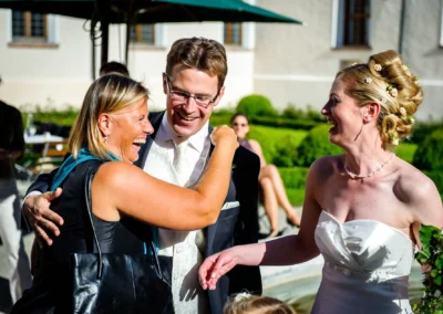 Brautpaar lacht mit Gast im Kloster Seeon bei sonniger Hochzeitsfeier. Hochzeitsreportage in Oberbayern.