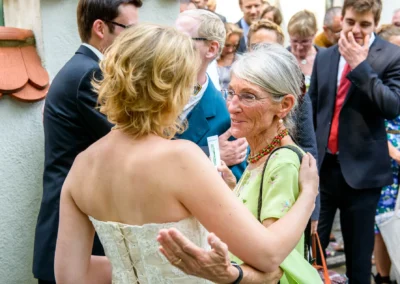 Braut umarmt aeltere Frau bei Hochzeit in Muenchen. Hochzeitsreportage mit Gaesten in festlicher Kleidung.