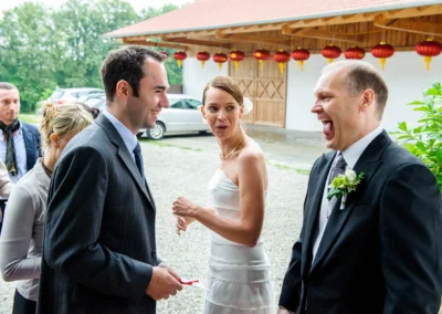 Hochzeitsgesellschaft lacht bei einer Feier in Oberbayern mit chinesischen Laternen im Hintergrund. Hochzeitsfoto.