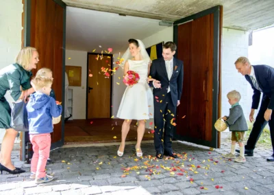 Brautpaar verlässt Kirche, bunte Blumenblätter werden geworfen. Hochzeitsfoto in Feldafing am Starnberger See.