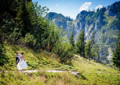 Brautpaar auf Waldweg bei Hochzeit im Chiemgau, vor beeindruckender Bergkulisse, aufgenommen von Hochzeitsfotograf.