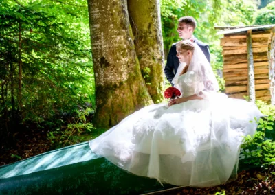 Brautpaar sitzt auf gruenem Kanu im Wald bei Hochzeitsfotos nahe Grainau, Hochzeitsfotografie im Freien.