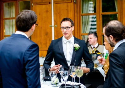 Gesellschaft bei Hochzeit im Margarethenhof, eleganter Mann im Frack spricht mit Gaesten. Hochzeitsfotografie vor Ort.
