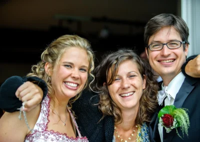 Lächelndes Brautpaar mit Gast bei Hochzeitsreportage am Walchensee. Hochzeitsfotografie zeigt Freude und Gemeinschaft.