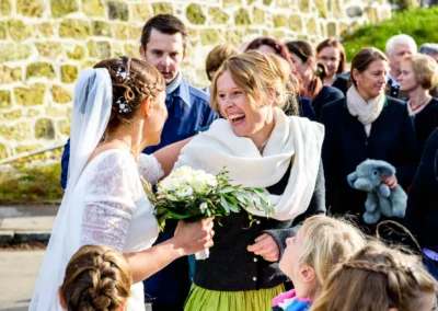 Braut lacht mit Freundin vor einer Gruppe von Gaesten, Hochzeitsfotografie in Valley-Unterdarching nahe Holzkirchen.