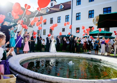 Bei einer Hochzeitsreportage am Kloster Seeon lassen Gaeste rote Herzballons steigen, Feier nahe Chiemsee.