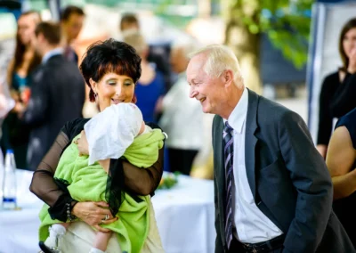 Mann und Frau lachen, dabei ein Baby haltend. Hochzeitsreportage bei der evangelischen Friedenskirche Starnberg.