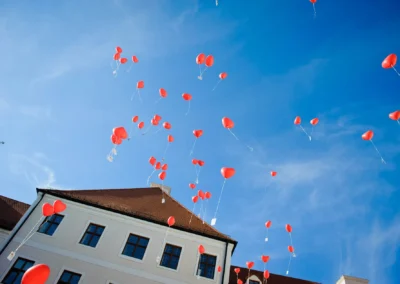 Rote Herzballons fliegen bei einer Hochzeit im Kloster Seeon glücklich in den blauen Himmel.