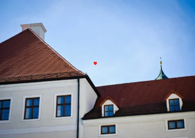 Gebaeude mit roten Daechern und rotem Herzballon am Himmel. Hochzeit bei Kloster Seeon im Chiemgau.