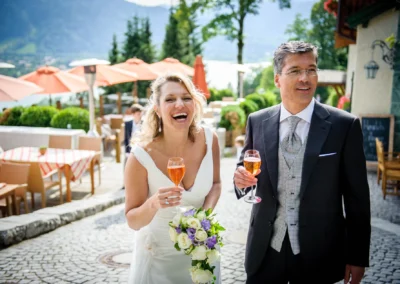 Brautpaar lacht beim Anstoßen mit Sektgläsern im Leeberghof Tegernsee. Hochzeitsreportage zeigt Freude und Feier.