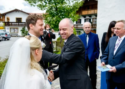 Brautpaar begruesst Gaeste bei kirchlicher Trauung in Schaftlach. Festliche Hochzeitsszene mit Laecheln und Freude.