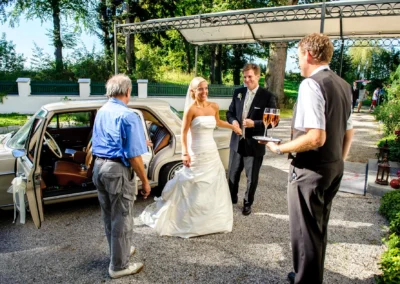 Brautpaar an einem Oldtimer vor Schlossgut Oberambach, mit Kellner im Anzug, Hochzeitsfotografie Moment.