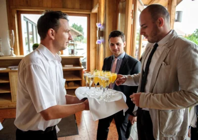 Kellner serviert bei einer Hochzeitsreportage in Sauerlach-Arget Sekt und Orangensaft an elegant gekleidete Gaeste.