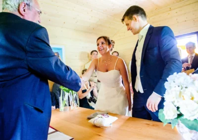 Braut und Brautigam beim Handschlag mit einem Gast auf Hochzeit am Eibsee. Hochzeitsfotografie und -reportage.
