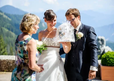 Brautpaar mit Geschenk bei Hochzeit in Oberbayern, Bergkulisse im Hintergrund. Hochzeitsfoto nahe des Chiemsees.