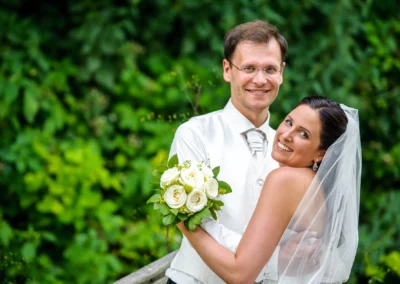 Brautpaar umarmt sich mit Blumenstrauss im Gruenen in Wolfratshausen, festgehalten in Hochzeitsfotografie.