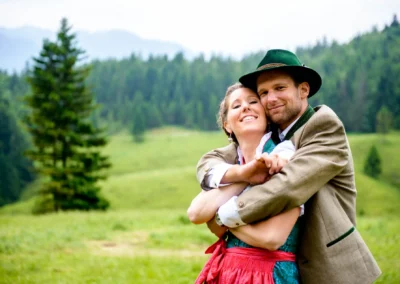 Brautpaar in traditioneller Tracht laechelt im Gruenen, Hochzeitsfoto am Sillberghaus in Oberbayern.