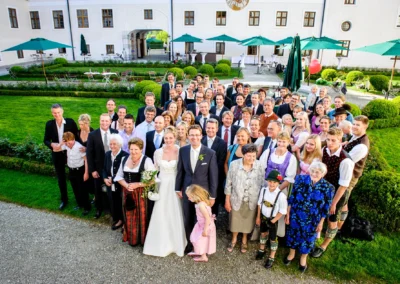 Hochzeitsfoto im Kloster Seeon: Brautpaar und Gaeste im Garten. Festliche Kleidung und fröhliche Gesichter am Chiemsee.