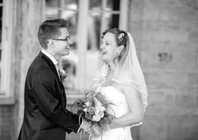 Brautpaar lacht bei Hochzeitsreportage in Starnberg. Er haelt ihre Haende, sie traegt Blumen und einen Schleier.