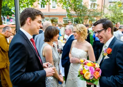 Hochzeitsgesellschaft lacht bei Hochzeit in München Schwabing, Brautstrauss in lebhaften Farben. Hochzeitsfoto.