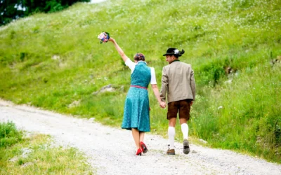 Brautpaar in traditioneller Tracht spaziert auf Weg in Oberbayern bei Bayrischzell, Brautstrauss hochhaltend. Hochzeitsfoto.