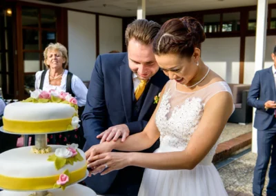 Brautpaar schneidet Hochzeitstorte bei Feier, fotografiert nahe Schliersee, elegant dekoriert mit Blumenornamenten.