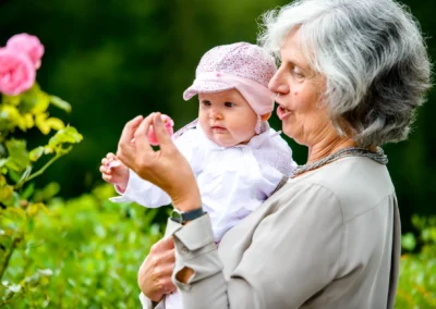 Großmutter mit Baby bei einer Hochzeit nahe Tegernsee, umgeben von rosa Blumen und Gruen. Hochzeitsfoto mit natuerlichem Charme.