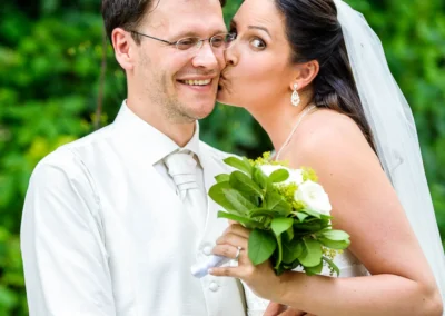 Brautpaarfoto auf der Sprengoeder Alm, Braut mit Blumenstrauss kuessen sich, festgehalten in Hochzeitsfotografie.