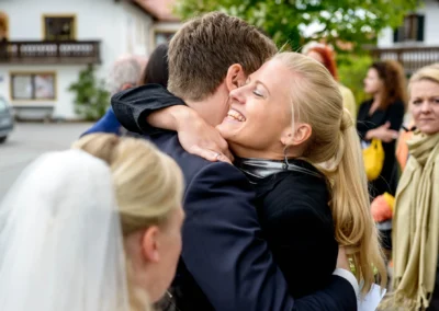 Umarmung bei kirchlicher Trauung in Schaftlach, laechelnde Gaeste draussen nach Hochzeitszeremonie.