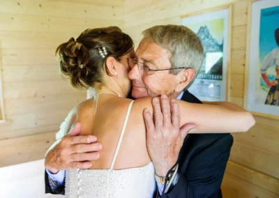 Braut umarmt älteren Mann während der Hochzeit am Eibsee. Emotionale Hochzeitsfotografie in rustikalem Ambiente.