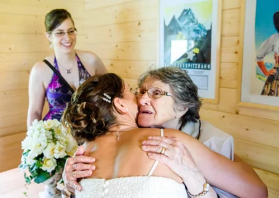 Braut umarmt ältere Dame bei Hochzeit am Eibsee, Hochzeitsfotografie mit emotionalem Moment, Holzdekor im Hintergrund.