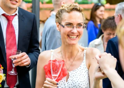Lächelnde Frau mit Brille bei einer Hochzeitsfeier in Muenchen, bei Hochzeitsreportage mit Sektglas.