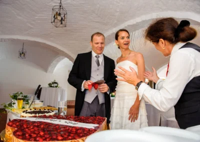 Brautpaar und Gaeste bei Hochzeit in Gut Thurnsberg, Hochzeitstorte im Vordergrund, festlicher Saal im Hintergrund.