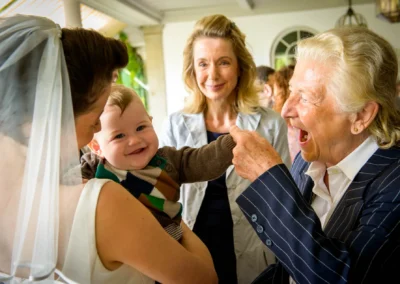 Mutter mit Baby bei Hochzeit in Feldafing, laechelnde Gaeste. Hochzeitsfotografie festgehalten im Hotel Kaiserin Elisabeth.