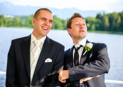 Zwei Männer in Anzügen lachen bei der Hochzeit auf einem Schiff am Staffelsee. Hochzeitsreportage.