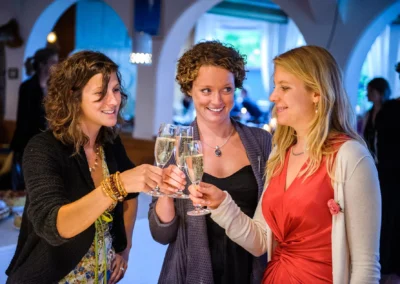 Drei Frauen stoßen bei einer Hochzeitsfeier im Strandcafe Bucherer mit Sekt an. Hochzeitsfotografie in München.