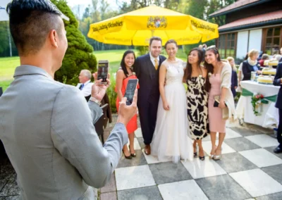 Gaste posieren fur ein Hochzeitsfoto im Aurachhof mit gelbem Sonnenschirm im Hintergrund. Hochzeit nahe Fischbachau.