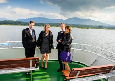Gäste bei einer Hochzeit auf einem Schiff am Staffelsee. Hochzeitsfoto mit Seeblick und Bergen im Hintergrund.