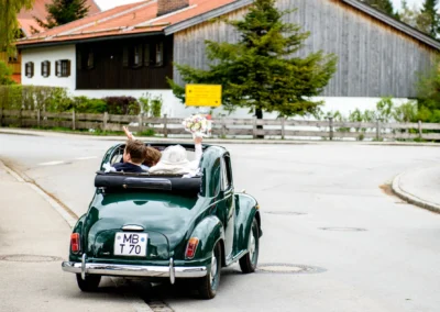 Brautpaar in einem Oldtimer nach der Trauung in Schaftlach, Hochzeitsfotografie im Gruenen.
